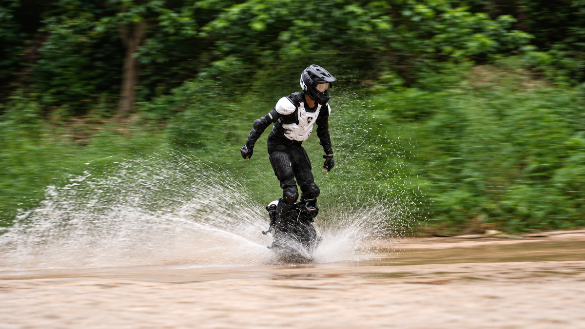 A rider in protective gear rides an electric unicycle through a spray of water on a course.