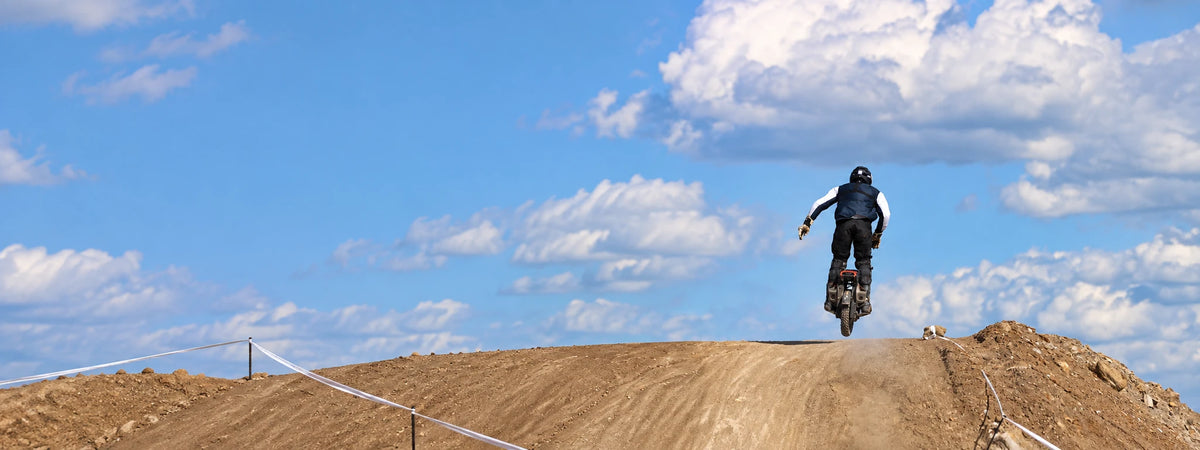 KingSong electric unicycle rider airborne over visible dirt race course, desktop wide hero